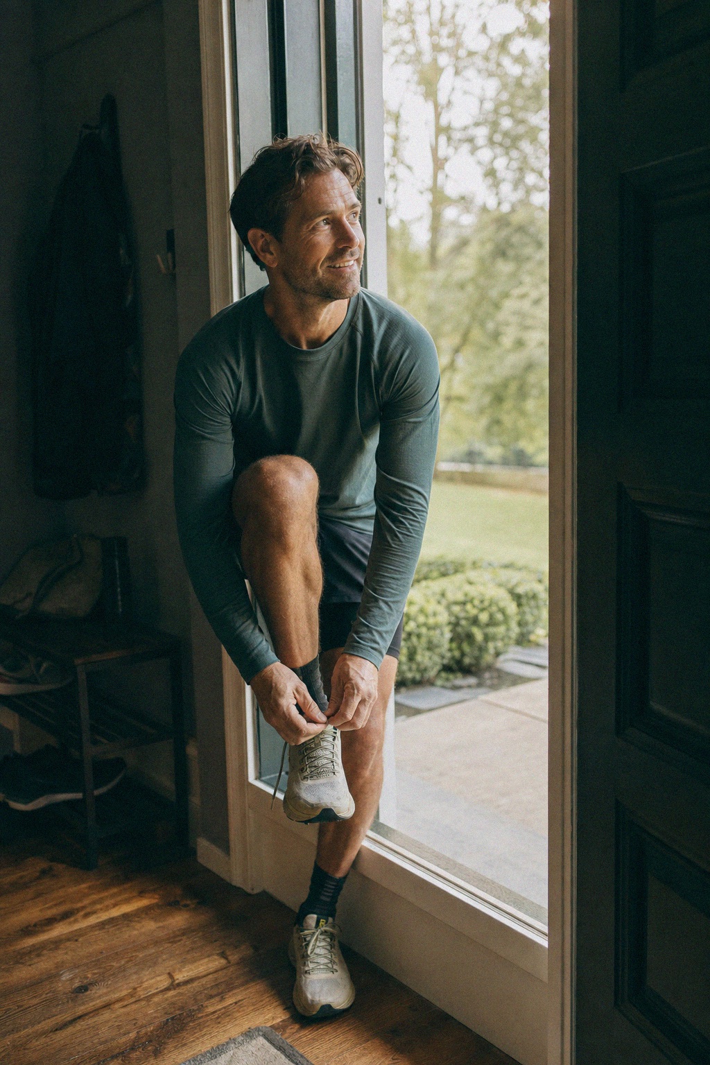 Man lacing his running shoe in a doorway, ready to start his morning run